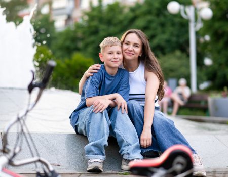 Happy mother and teenage son sitting hugging near fountain in ur