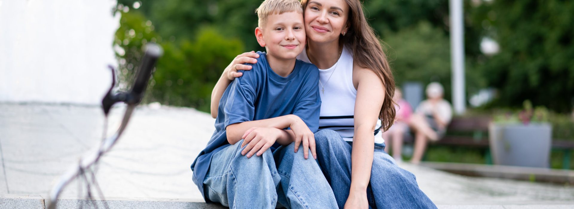 Happy mother and teenage son sitting hugging near fountain in ur