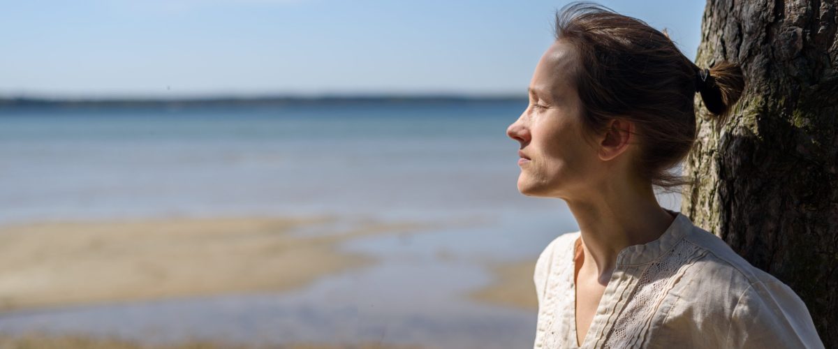 Kobieta siedząca między drzewami i patrząca na morze