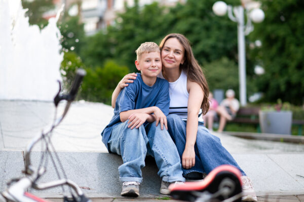 Happy mother and teenage son sitting hugging near fountain in ur
