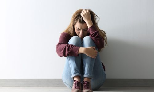 Front view full body portrait of a sad woman sitting on the floor at home